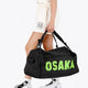 Osaka sports duffel bag in black with logo in green. Woman holding the bag