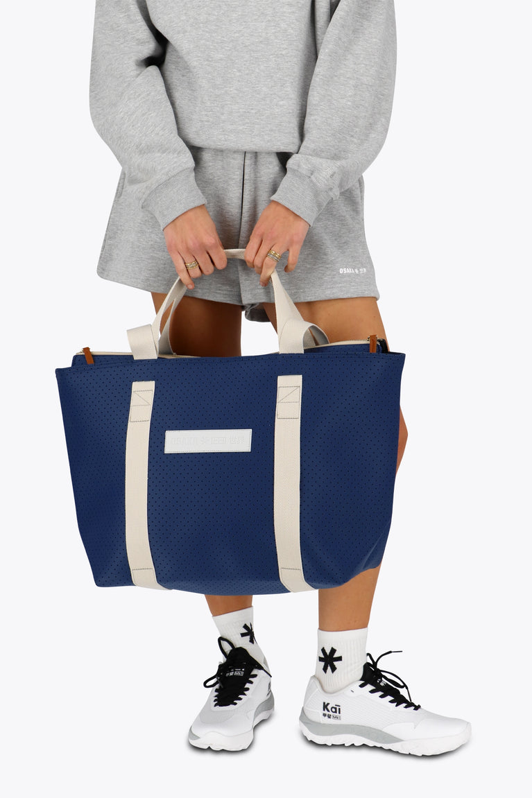 Osaka neoprene Tote bag in navy with structure and logo in white. Woman holding the bag