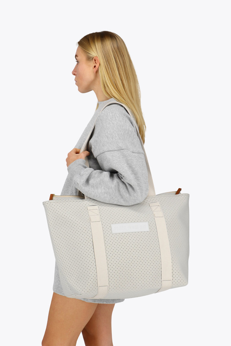 Osaka neoprene Tote bag in light grey with structure and logo in white. Woman wearing the bag