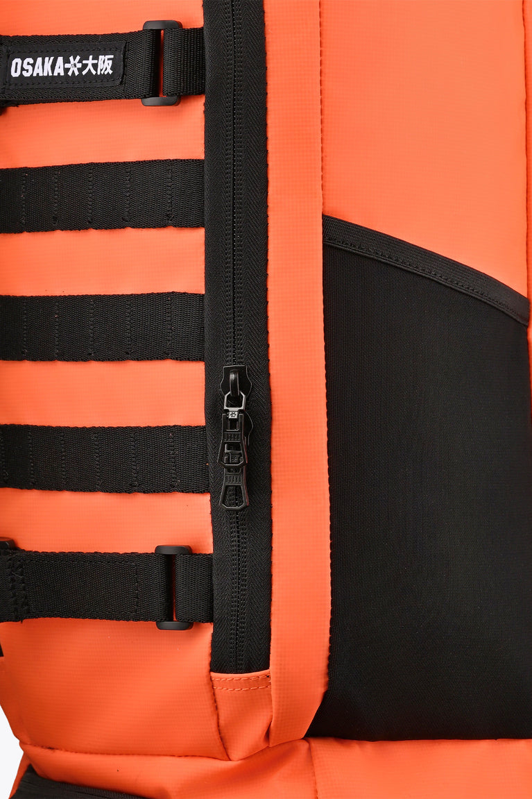 Close-up of orange stickbag panel with zipper, black harness straps and webbing.