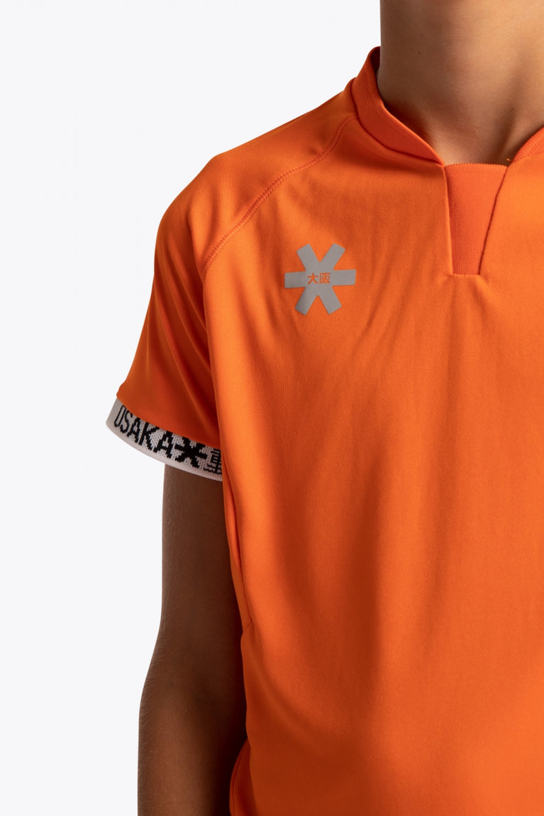 Boy wearing the Osaka Kids Jersey in Orange. Front detail logo view