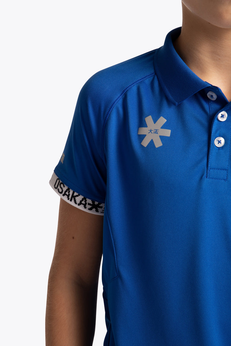 Boy wearing the Osaka Kids Polo Jersey in Royal blue. Front detail logo view