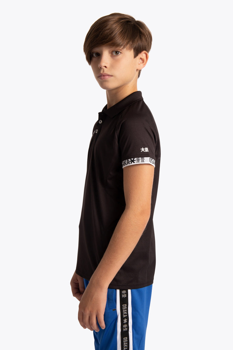 Boy wearing the Osaka Kids Polo Jersey in Black. Side view