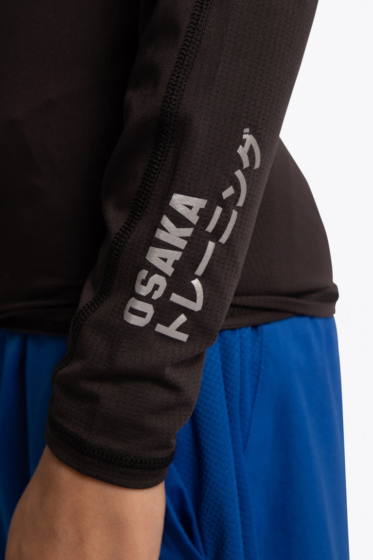 Kid wearing the Osaka Kids Baselayer Top in Black. Front detail logo sleeve view