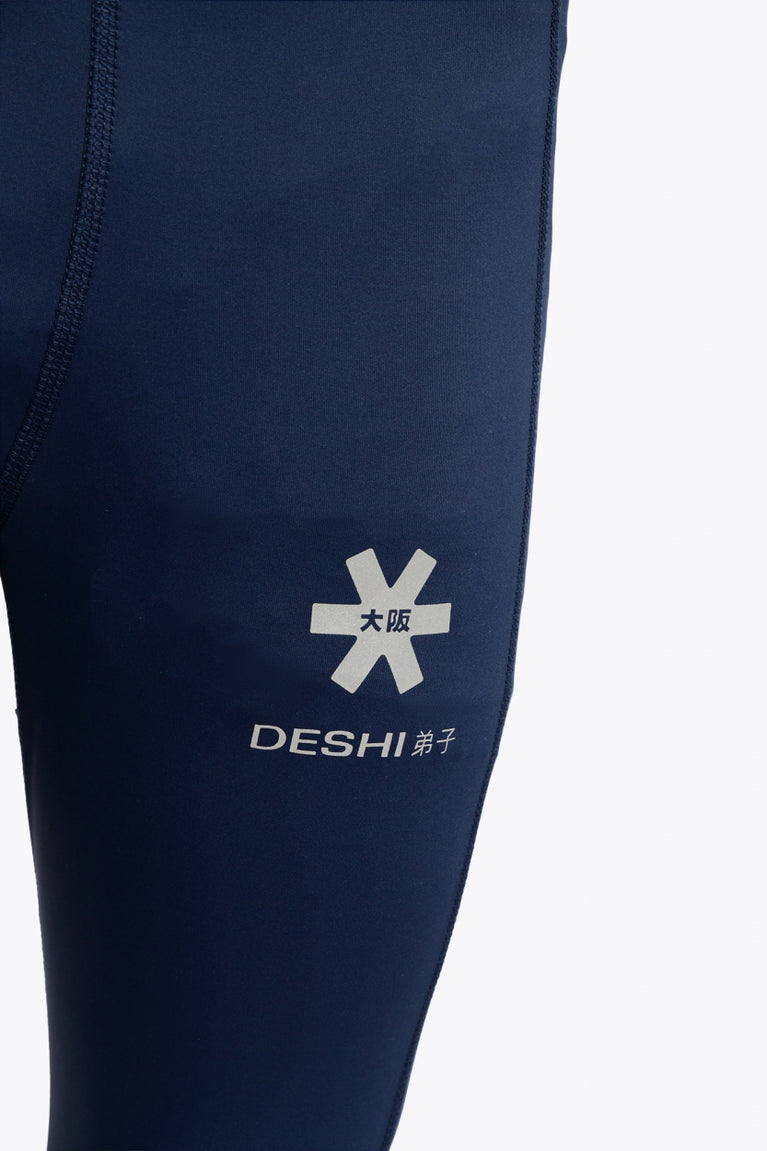 Model wearing the Osaka Kids Baselayer Tights in Navy. Detail front logo view