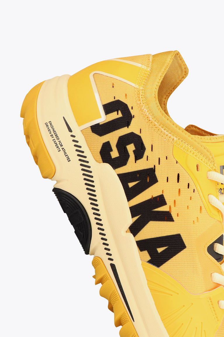 Honey Comb yellow colour Osaka Ido Mk1 shoe Performance hockey shoe for an edge over competition. Made with fast drying mesh upper, strategical cleat composition, heel deceleration, Ankle lock lacing option and with a footgrabbing/stabilizing eyestay system. Close-up side view photo